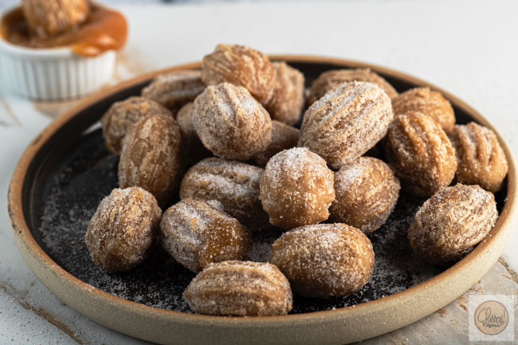 Varias unidades de mini churros recheados com doce de leite em um prato marrom.