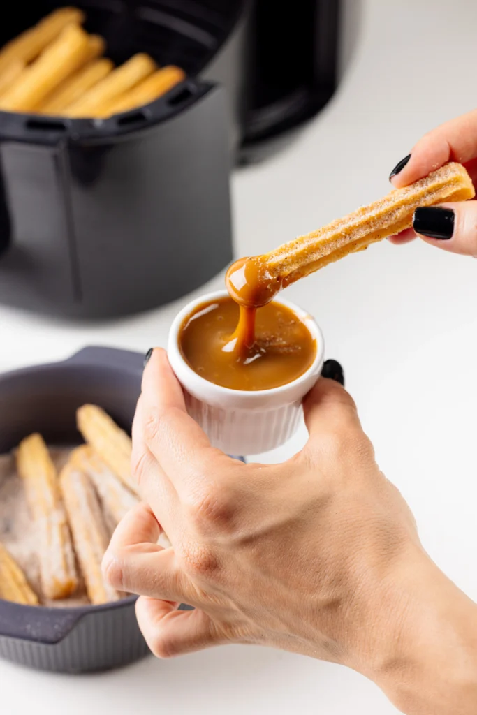 Churros Espanhóis – 10 cm sendo colocados em um potinho com doce de leite.