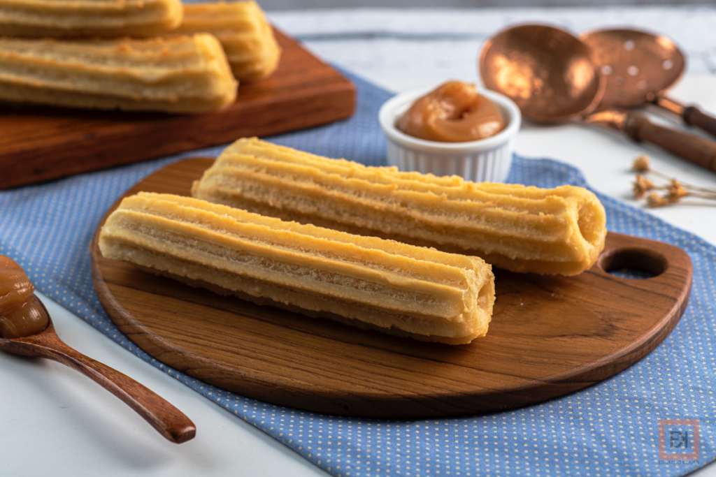 Duas unidades de churros tradicionais 16 cm, em uma tábua de madeira.