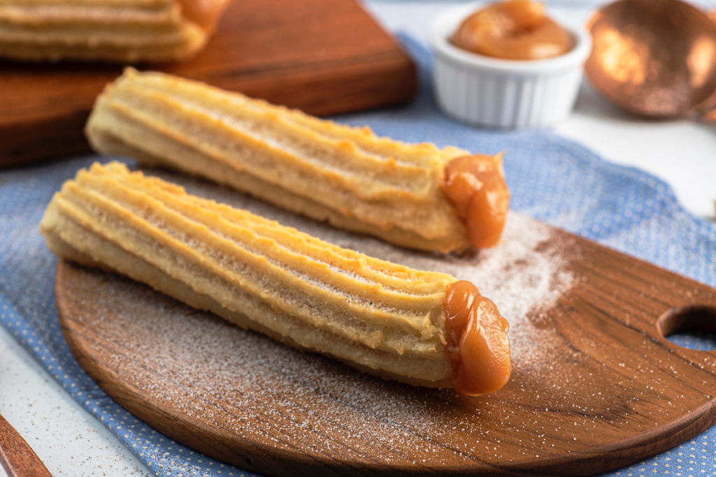 Dois churros tradicionais gourmet - 16 cm em um prato marrom e recheio de doce de leite.