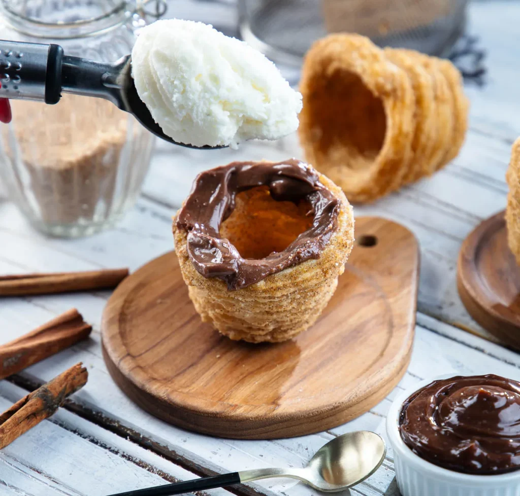Cestinha de churros com Nutella em cima, uma colher de sorvete sendo colocada dentro.